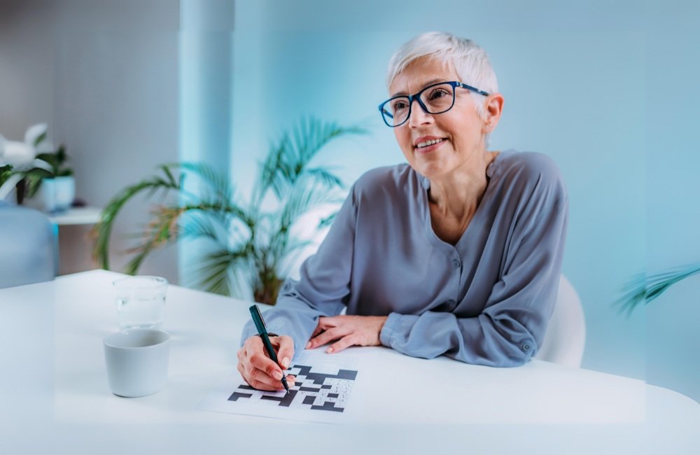 Atividades cognitivas para idosos. Foto com uma senhora de óculos preenchendo um caça palavras.