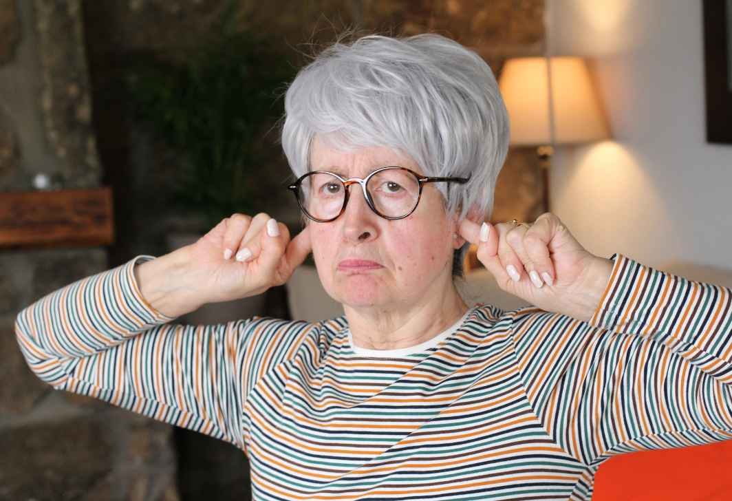 Teimosia dos pais idosos, descubra nesse post como lidar com a teimosia dos pais idosos. A imagem tem uma senhora idosa tampando o ouvido com os dedos das mãos.